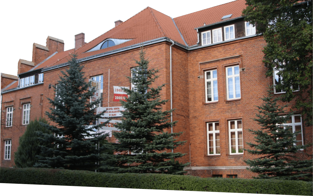 budynek szkoły z czerwonej cegły w otoczeniu zielonych drzew